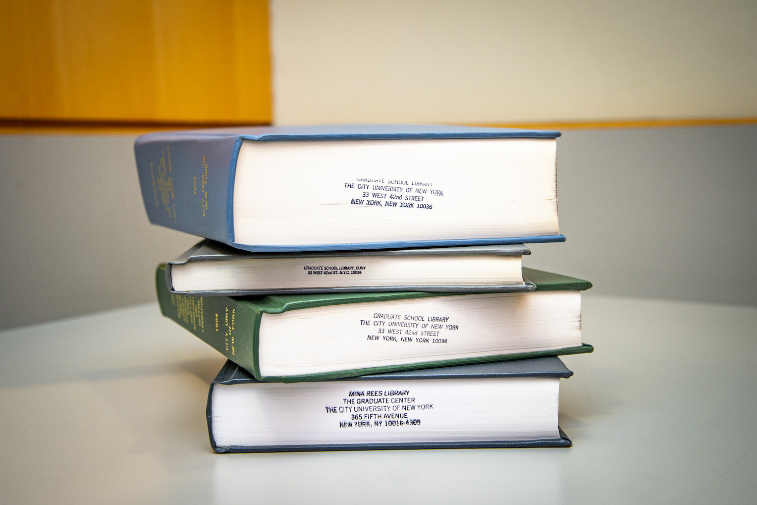 A stack of books stamped with contact information for CUNY Graduate Center Library